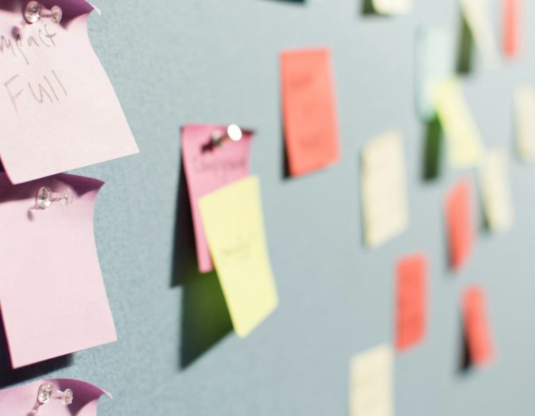 Bunte Haftnotizen an einer grauen Wand, verschiedene Farben und Formen.